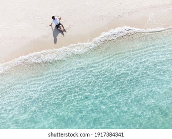 Young Man Sitting And Relaxing At Beautiful Tropical White Sand Beach With Wave Foam And Transparent Sea, Summer Vacation And Travel Background Top View From Drone