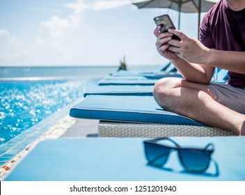 Young Man Sitting  Resting And Using Smart Phone At The Swimming Pool. Summer Holiday Traveling Concept Design Banner With Copyspace.