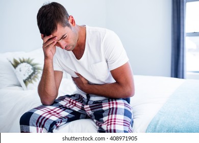 Young Man Sitting With Stomach Pain On Bed In Bedroom