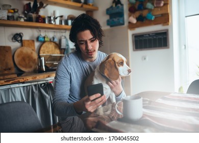 Young Man Sitting Table With His Dog And Using Mobile Phone