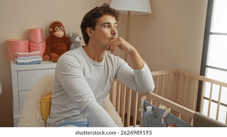 Young man sitting thoughtfully in a cozy bedroom next to a baby's cradle, surrounded by soft toys and pastel decor, creating a serene interior atmosphere at home.