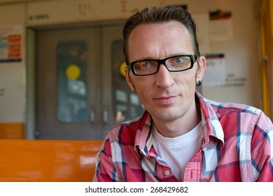 Young man sitting in train commuting to work looking in camera