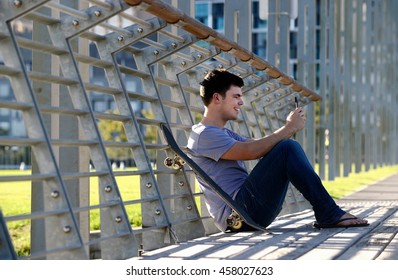 Young man sitting, using mobile phone, skateboard beside him