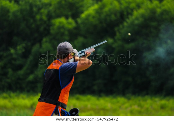 Young man skeet\
shooting outdoors; shooting clay pigeon targets at gun club with\
airborne casing and copy\
space