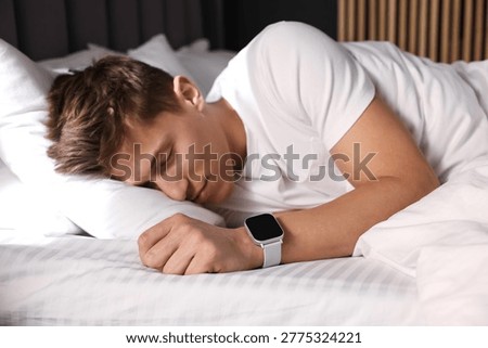 Young man with sleep tracker sleeping on bed at home