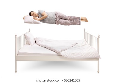 Young Man Sleeping And Floating Above A Bed Isolated On White Background