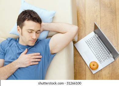 Young Man Sleeping On Sofa At Home, Laptop On Floor.  Overhead View.