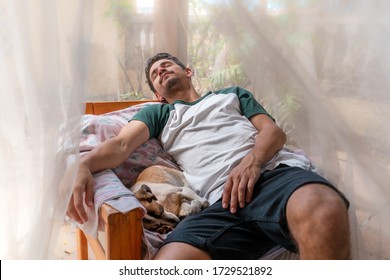 young man sleeps in an armchair in the garden under a mosquito net. A dog sleeps beside him