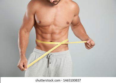 Young Man With Slim Body Using Measuring Tape On Grey Background, Closeup View