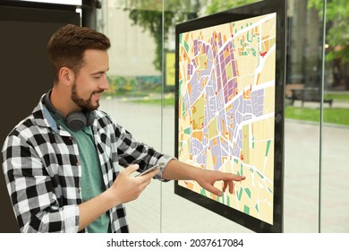 Young Man With Smartphone Near Public Transport Map At Bus Stop