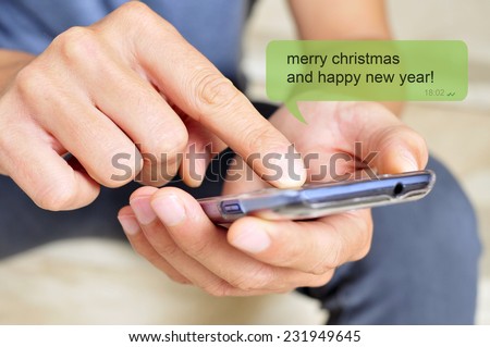 a young man with a smartphone and the text message merry christmas and happy new year in a chat bubble