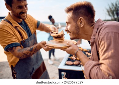 Young man smelling fresh hamburger made by his friend during barbecue party in the backyard. - Powered by Shutterstock