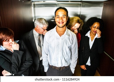 A young man smiles in embarrassment in an elevator while people hold their noses.
