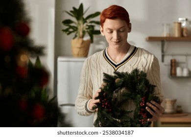 A young man smiles as he holds a beautifully adorned Christmas wreath while decorating at home. - Powered by Shutterstock