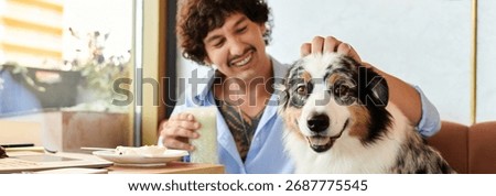 A young man smiles warmly while petting his dog, enjoying drinks and snacks inside a cozy cafe.