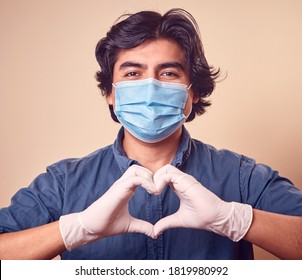 A Young Man Smiles While Wearing Nitrile Gloves With A Surgical Mask On His Face. Long Hair Man. Gloved Hands Making Heart Shape.