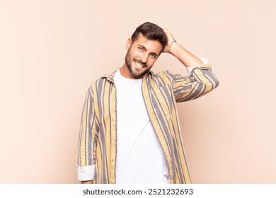 young man smiling cheerfully and casually, taking hand to head with a positive, happy and confident look