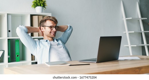 Young man smiling as he reads the screen of a laptop computer while working on a comfortable place by the wooden table at home. Happy Social distancing concept