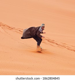 Young man smiling, sand dune surfing wearing bisht - traditional Bedouin coat. Sandsurfing is one of the attractions in Wadi Rum desert - Powered by Shutterstock