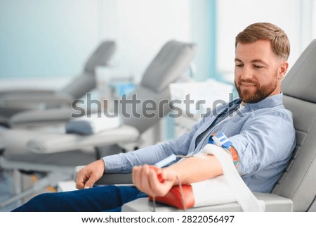 Young man smiling while donating blood in a modern clinic. Concept of altruism, health care, and saving lives