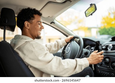 A young man smiling while driving, holding his phone in a car mount