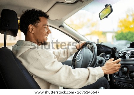 A young man smiling while driving, holding his phone in a car mount