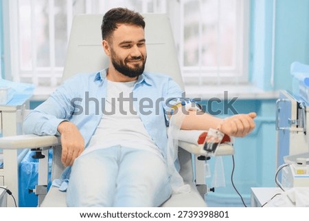 Young man smiling while giving blood, contributing to healthcare and medical support in a clean clinic environment