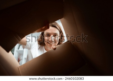 Young Man Smiling While Looking Inside Cardboard Box, Capturing A Moment Of Joy And Anticipation In A Casual Setting