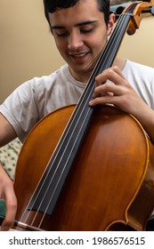 young man smiling while playing a piece of music with the cello inside his house as a rehearsal and learning vertical photo