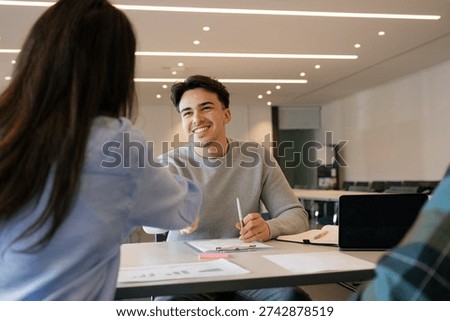 Young man smiling while shaking hands across a desk with a colleague in an office, celebrating a successful job interview, hiring decision or new professional partnership