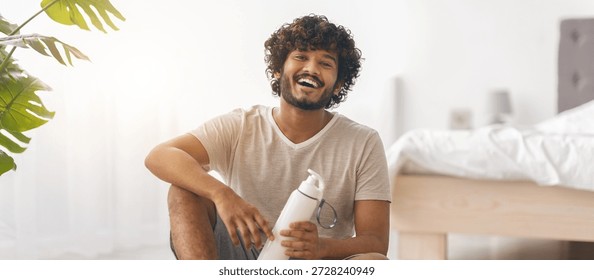 Young Man Smiling While Sitting on the Floor With a Water Bottle in a Bright Room