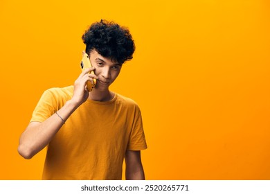 Young man smiling while talking on a yellow phone against a vibrant yellow background, showcasing a playful and modern lifestyle Emphasizes communication and social interaction - Powered by Shutterstock