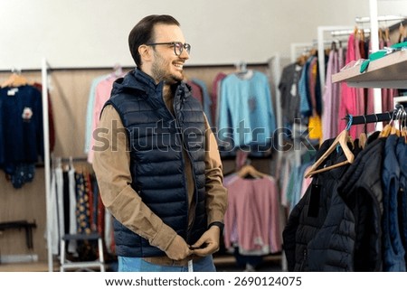 Young man smiling while trying on a trendy padded puffer vest in a modern boutique, enjoying the shopping experience