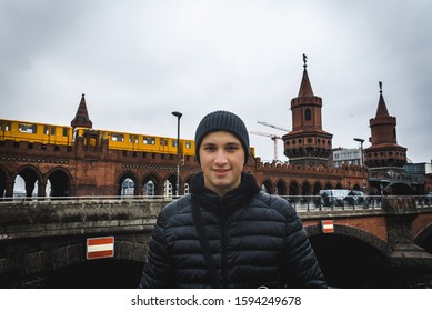 Young man in smilling with Oberbaum Bridge and yellow train on background in cloudy weather in Berlin. Travel and tourism in Berlin concept. Europe travel in winter. Student and youth travel concept. - Powered by Shutterstock