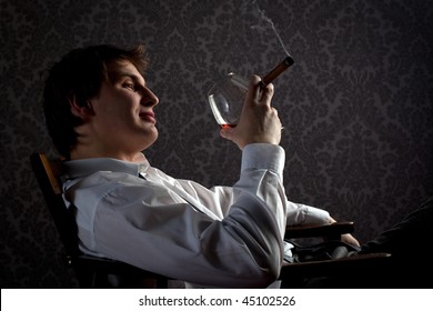 Young Man Smoking Cigar And Drinking Cognac At Night