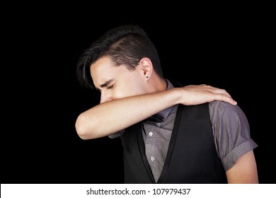 A Young Man Sneezing Into His Elbow.  Black Background.