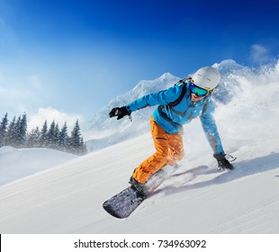 Young man snowboarder running down the slope in Alpine mountains. Winter sport and recreation, leisure outdoor activities.