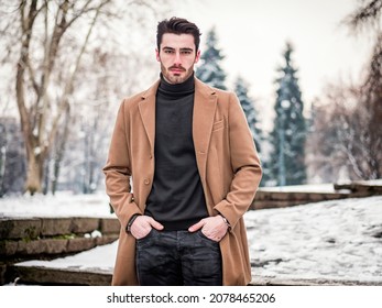 Young Man In Snowy City Park Wearing Wool Coat, Looking At Camera