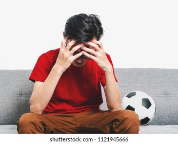 Young Man Soccer Fan Crying Face After Watching Football Match On Tv While Sitting On Grey Sofa And Wearing Red Shirt Short Sleeve.