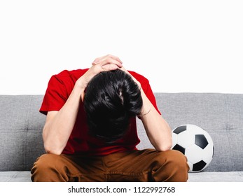 Young Man Soccer Fan Crying Face After Watching Football Match On Tv While Sitting On Grey Sofa And Wearing Red Shirt Short Sleeve.