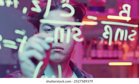 Young man solves mathematical equations on blackboard. Media. Young man solves complex equations on transparent board. Genius writes equations on blackboard in neon light