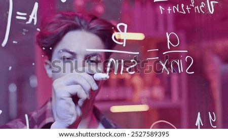 Young man solves mathematical equations on blackboard. Media. Young man solves complex equations on transparent board. Genius writes equations on blackboard in neon light