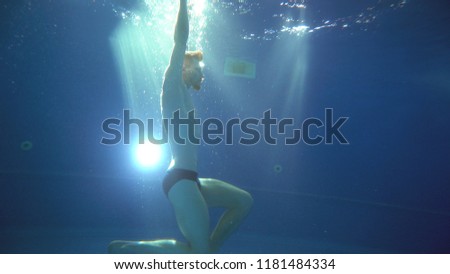 A young man somersaults and does a somersault under the water. He is posing in front of the camera. Underwater view.