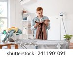 Young man sorting clothes near ironing board in laundry room