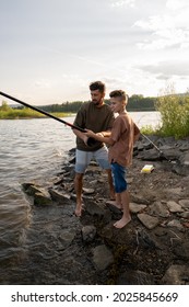 Young Man Spinning Wheel On Rod While Fishing With His Teenage Son