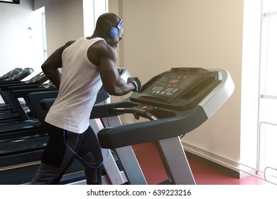 Young Man In Sportswear And Blue Headphones Running On Treadmill At Gym, , Side View