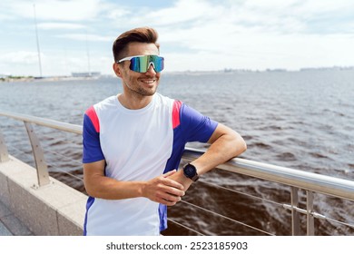 A Young Man in Sporty Attire and Sunglasses Enjoys a Sunny Day by the Waterfront With a View of the City Skyline in Summer - Powered by Shutterstock