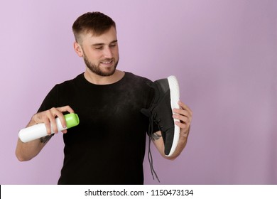 Young Man Spraying Air Freshener On Shoe Against Color Background