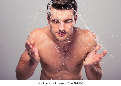 Young man spraying water on his face over gray background