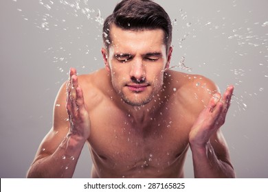 Young Man Spraying Water On His Face Over Gray Background